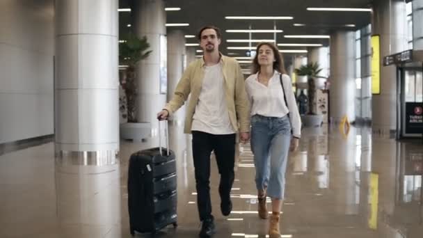 Gülümseyen bir çiftin birlikte havalimanında geziye ya da tatile gidişinin ön görüntüsü. Birlikte seyahat edin. Kot pantolonlu çekici beyaz bir kadın ve bavullu bir adam seyahat etmeye hazır. — Stok video