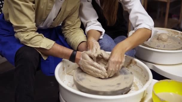 Schmutzige Pärchenhände aus nächster Nähe. Ein verliebtes romantisches Paar, das gemeinsam an Töpferscheibe und Tontopf arbeitet. Frau gießt Wasser, arbeitet zusammen in Bastelatelier-Werkstatt. Keine Gesichter — Stockvideo