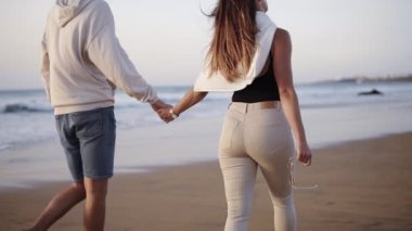Kumsalda genç evli bir çift romantik gündoğumunda el ele tutuşuyorlar. Kadın ve erkek tatil tatillerinde dinleniyorlar, günlük kıyafetler giyiyorlar. Ağır çekim. Nadir görünüm