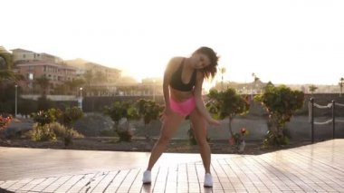 Dans eden seksi kız mı yoksa plajda pop dansı mı? Pembe şortlu, bronzlaşmış, uzun saçlı kadın vücudunu yerde hareket ettiriyor. Güzel bayan arka planda tropikal alanla tutkuyla dans ediyor. Mercek