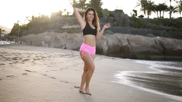 Mulher sensual com cabelos longos em shorts rosa e sutiã preto pela costa do mar rindo e flertando para a câmera. Menina sexy dança e ri em um humor alegre. Descanse junto ao mar em um dia ameno de verão — Vídeo de Stock