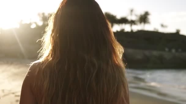 Zabawna młoda kobieta ciesząca się wakacjami na letniej plaży. Zmysłowa kobieta z wietrznymi włosami spaceruje po plaży w czarnym staniku nad morzem. Patrząc od ramienia, odwraca się do — Wideo stockowe