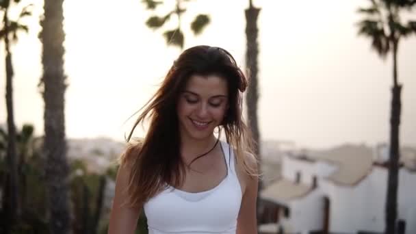 Portrait slow motion footage of a beautiful sporty girl walking by street beyond palm trees around. Calm walk by street, carefee girl smilling walks around. Wind blowing her hair. Freedom, vacation — Stock Video