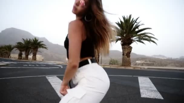 Сексуальная девушка с красивым телом, танцующая танец на курорте, в районе Аль. Девушка в солнечных очках двигает задницей, стоя на асфальте. Брюнетка передвигает свое тело на улицу. — стоковое видео
