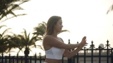 Beyazlar içindeki sportif kadın yürüyerek ısınıyor, elleri havada. Beyaz tenli, uzun saçlı, sokaklarda palmiye ağaçlarıyla dolaşıyor. Yan görünüm