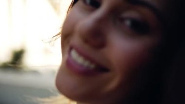 Arka planda palmiye ağaçları ve rüzgarda dalgalanan saçlarıyla yürüyen ve kameraya bakan esmer genç kızı yakından çek. Yaz zamanı. Yolculuğun keyfi. Omzunun üstünden bakıyorum. Portre