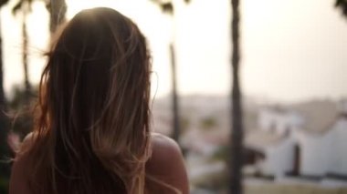 Yalnız tatil hayatı. Beyaz spor sutyen giyen esmer kadın bakış açısında nadir görülür. Yüksek uçurumdan tropikal tatil köylerine bak. Seyahat güzergahı. Rüzgâr saçlarını savuruyor