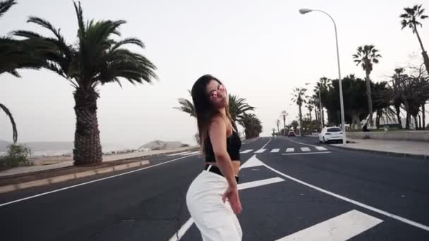 Sexy girl with beautiful body dancing twerk at the resort, tropical area right on the road. Girl in sunglasses moves her butt standing on the asphalt. Brunette girl moves her body outdoors. Front view — 비디오