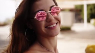 Güneş gözlüklü neşeli bir kadın palmiye ağaçlarıyla parkta yürüyor, elinde sarı külahlı dondurma var. Ağır çekim. Genç ve çekici bir kadın, açık havada güneşli yeşil bir yaz gününde dondurmanın tadını çıkarıyor. poz