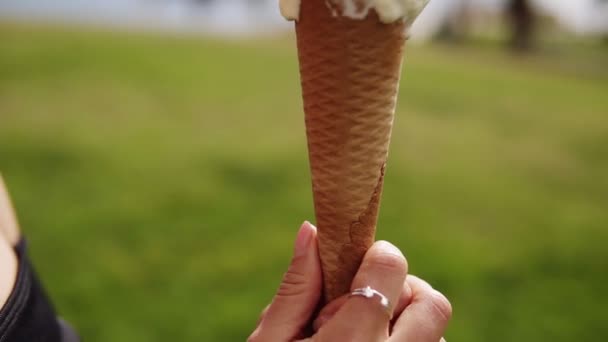 Gros plan mignon brunette sensuelle fille lécher la crème glacée sur un cône blanc et jaune scoops. En regardant dans la caméra et en souriant. Capturé en vue latérale. Vert à l'extérieur — Video