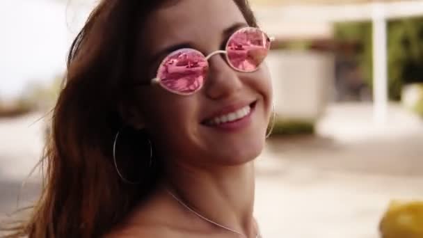 Joyful woman in sunglasses walking in the park with palm trees, holding yellow cone ice cream. Slow motion. Young attractive woman enjoying tasty ice cream in the green sunny summer outdoors. posing — Stock Video