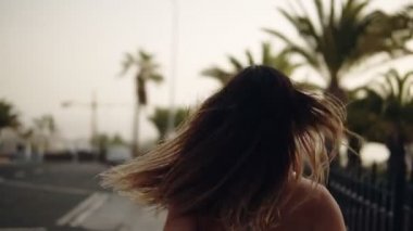 Asfalt yolda koşan, beyaz spor kıyafetleriyle palmiye bahçesinde koşan bir kadın. Dışarıda koşan kadın. Palmiye ağaçlarıyla park et. Nadir bir manzara. Bulanık arkaplan