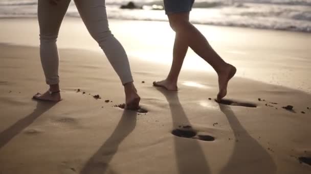 Casal relaxante andando descalço na praia.Eles estão passando tempo juntos, deixando pegadas na areia molhada, de mãos dadas. Pôr-do-sol suave no fundo. Vista rara — Vídeo de Stock