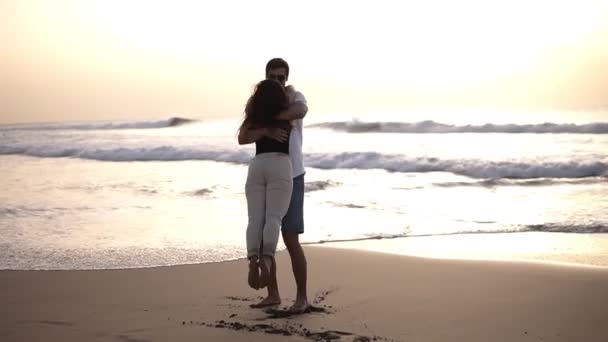 Young beautiful couple walking by the sea. Boy and girl. They are happy. Tall guy takes the tiny girl in his arms and turns her around. Silhouettes on an ocean background — Stock Video