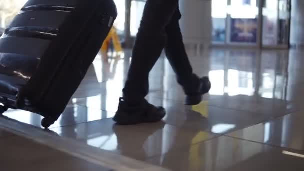 Zblízka, oříznutý záběr mužských nohou s černým zavazadlem kráčející na letiště terminálu. Zpomalený pohyb — Stock video
