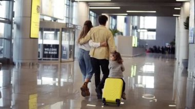 Modern Kafkas ailesinin - anne, baba, kız - havaalanı koridorunda yürürken ve tatilden önce kızlarını bavulla gezerken. Yavaş çekim