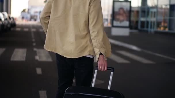 Zblízka, oříznutý záběr ženatého muže s černým zavazadlem kráčejícího po silnici k venkovnímu letišti. Zpomal. Vzácné zobrazení — Stock video