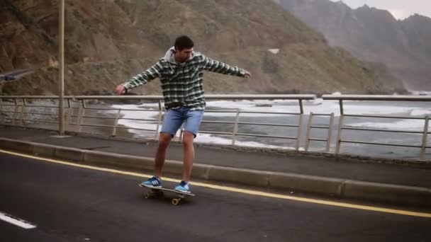 Esporte, estilo de vida, extremo e conceito de pessoas - Alto cara montando longboard pela estrada litoral em tempo nublado. Comprimento total de um homem ativo se exercitando na estrada. Movimento lento. Tempo nublado — Vídeo de Stock