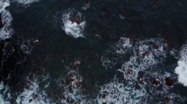 Zaman ayarlı. Mavi bir okyanustaki kayaların üzerinde havadan görünen dalgalar kırılıyor. Deniz dalgaları güzel sahil manzaralı insansız hava aracı görüntüsü. Okyanus dalgaları köpürüyor, ufukta gün doğumu beliriyor.