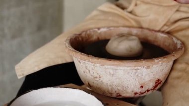 Atölyedeki kadın sanatçı çömlekçi seramik ürün yapıyor. Çarkın üzerindeki kil parçasına su sıçratan bir kadın. Yaratıcı atölye. Yavaş çekim