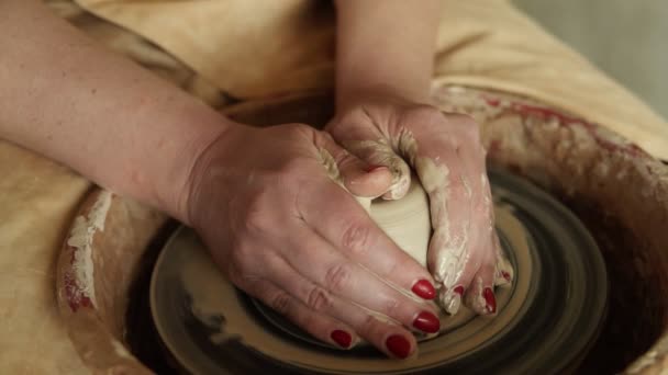 Primer plano de manos de alfareros con manicura roja trabajando con arcilla húmeda en una rueda de cerámica haciendo un producto de arcilla en un taller. Persona femenina irreconocible. Movimiento lento — Vídeo de stock