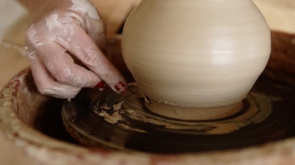 Vista frontal de las manos femeninas trabajan con arcilla en una rueda de alfarero. Potter moldea el producto de arcilla con herramientas de cerámica en la rueda de alfarería. De cerca. Artesanía fina y creación de objetos elegantes — Vídeo de stock