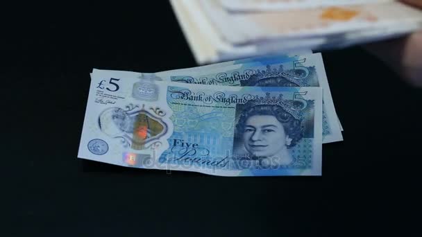 Person counts the money. Close-up of a female hands counting pounds banknotes GBP of different denomination. Five, ten, twenty pounds bills are roughly stacked. Black background. — Stock Video