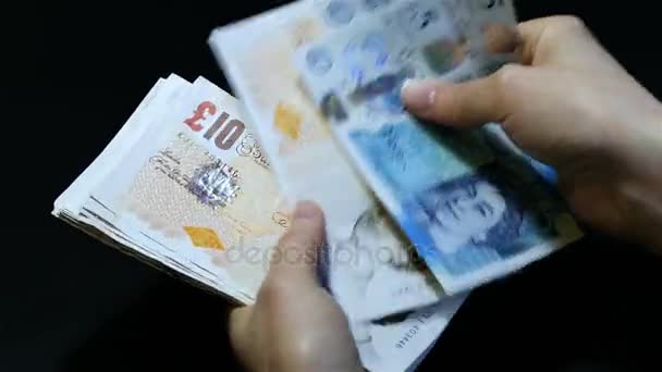 Orang menghitung uang. Close-up of a female hands counting pounds banknotes GBP of different denomination. Lima, sepuluh, dua puluh pound dalam kemasan. Latar belakang hitam . — Stok Video