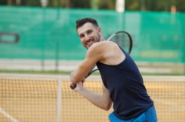 Mutlu genç adam Tenis kil sahada oynayan.