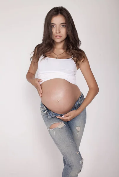 Mujer embarazada feliz con las manos en el estómago aisladas sobre fondo gris — Foto de Stock