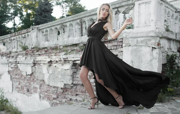 Giovane bella bella donna a piedi nel centro storico della città e guardando altrove. Elegante ragazza in abito nero in posa all'aperto — Foto Stock