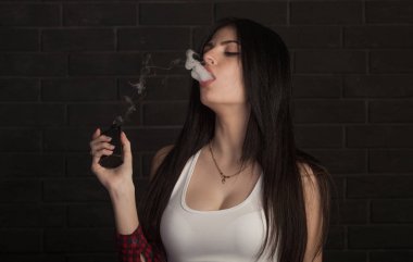 Genç güzel esmer kadın sigara, vaping e-sigara dumanlı siyah arka plan üzerine.