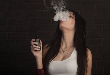 Genç güzel esmer kadın sigara, vaping e-sigara dumanlı siyah arka plan üzerine.