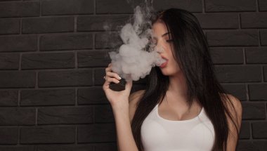 Genç güzel esmer kadın sigara, vaping e-sigara dumanlı siyah arka plan üzerine.