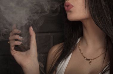 Genç güzel esmer kadın sigara, vaping e-sigara dumanlı siyah arka plan üzerine.