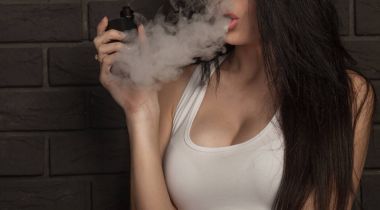 Genç güzel esmer kadın sigara, vaping e-sigara dumanlı siyah arka plan üzerine.