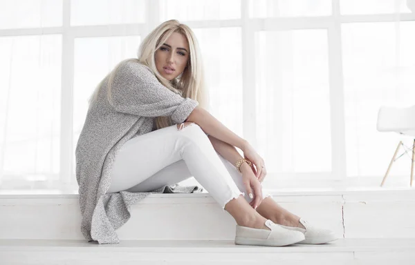 Porträt einer attraktiven, modischen jungen blonden Frau in weißen Jeans und grauem Mantel. — Stockfoto