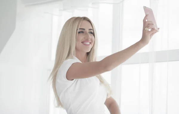 Beautiful smiling blonde business woman in white dress photographing selfie on a phone in her hands outdoors. copy space — Stock Photo, Image