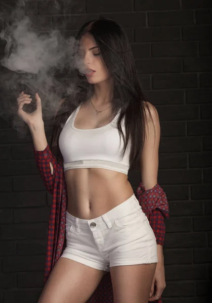 Giovane bella donna bruna fumare, vaping e-sigaretta con fumo su sfondo nero . — Foto Stock