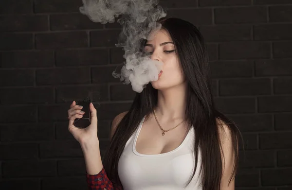 Joven hermosa morena fumando, vapeando e-cigarrillo con humo sobre fondo negro . — Foto de Stock