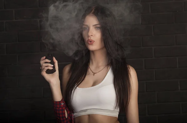 Молодая красивая брюнетка, курящая, испаряющая электронную сигарету с дымом на черном фоне . — стоковое фото