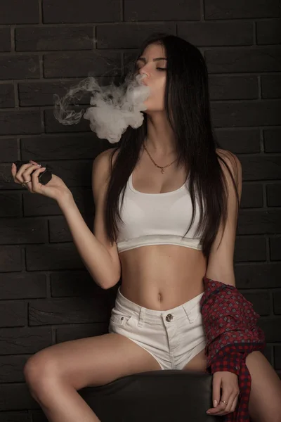 Joven hermosa morena fumando, vapeando e-cigarrillo con humo sobre fondo negro . — Foto de Stock