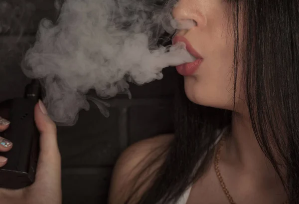 Joven hermosa morena fumando, vapeando e-cigarrillo con humo sobre fondo negro . — Foto de Stock