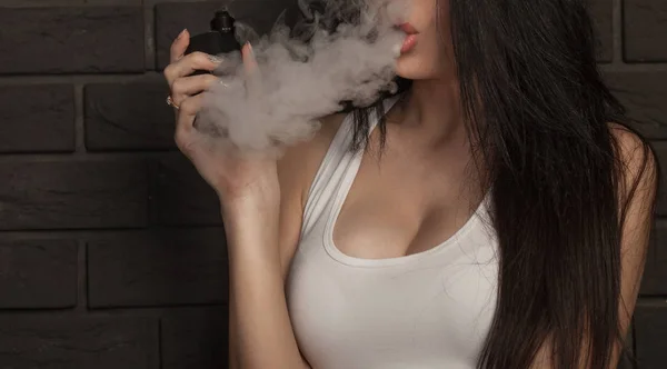 Joven hermosa morena fumando, vapeando e-cigarrillo con humo sobre fondo negro . — Foto de Stock