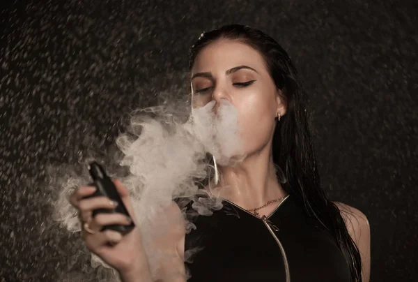 Joven hermosa mujer vapeando cigarrillo electrónico. Agua que fluye en la cara mujer . — Foto de Stock