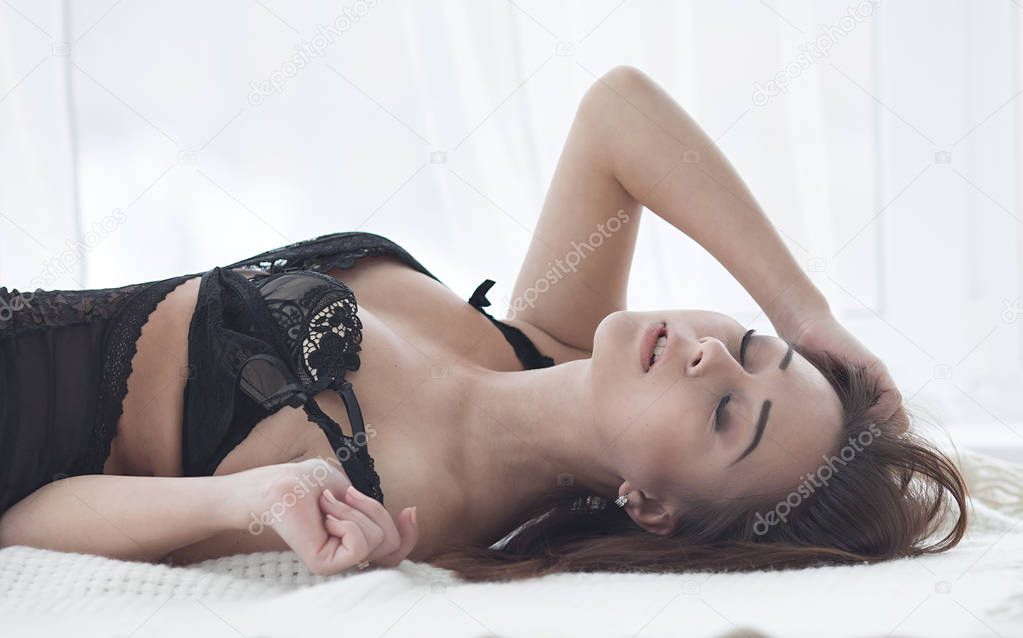 Sexy brunette woman with perfect beautiful shape of body in black erotic lingerie lying on bed
