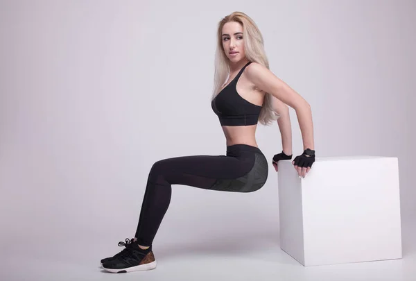 Blondýnka mladé pozitivní fitness trénink s bílé krychle. Štíhlá dívka sportovní oblečení. — Stock fotografie