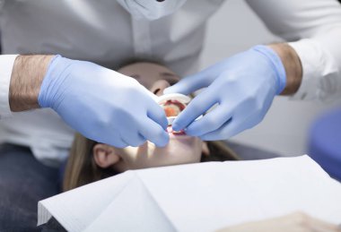 Diş telleri üzerinde balta ve ağız aynası ile çalışan ellere aşırı yakın çekim. Kadın ağzının makro kapağı diş tellerini gösteriyor.