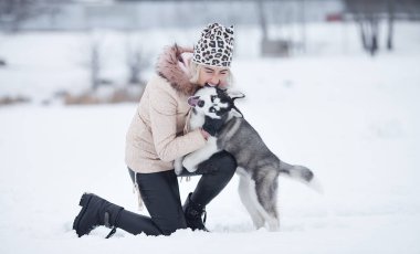Mutlu gülen Beyaz sarışın kadın ve köpeğini Husky. Kış beyaz ormandaki açık havada birlikte oynama.