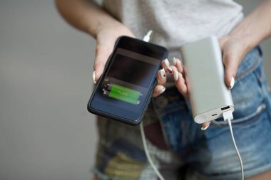 telefon ve şarj cihazı kız elele tutuşun. Powerbank ve smartphone kızın elinde. Enerji şarj cihazı gücü banka akıllı telefon. Natürmort modern dijital kavramı.